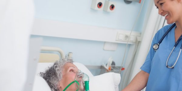 Nurse smiling to a patient while touching her hand in hospital ward